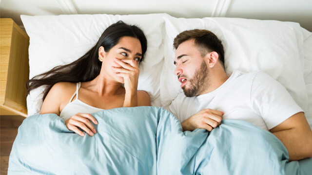 ベッドで口に手を当て眠るパートナーを横目で見る女性